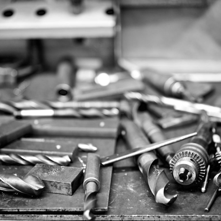 Drill bits Assorted metal tools, including drill bits and a chuck, scattered on a workbench.